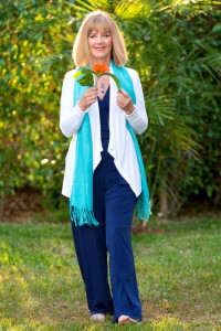 Jan Kinder-Key Note Speaker and Workshop Facilitator wearing a teal scarve, holding a tropical orange flower standing outside