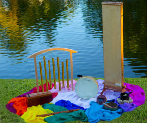 meditation musical instruments sitting on rainbow scarves against a grassy area and pond.