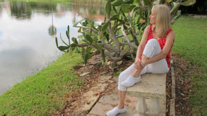 lady sitting on bench looking at pond wearing a red polkadot tank, reflecting thoughts next to tropical plants.