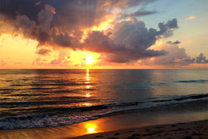 Waves against an orange sunset against an ocean and sandy beach.