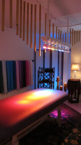 massage therapy table bed with windwchimes and lights rainbow colors above it.
