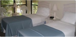 Two beds next to each other with wicker white furniture and blue bedspreads.