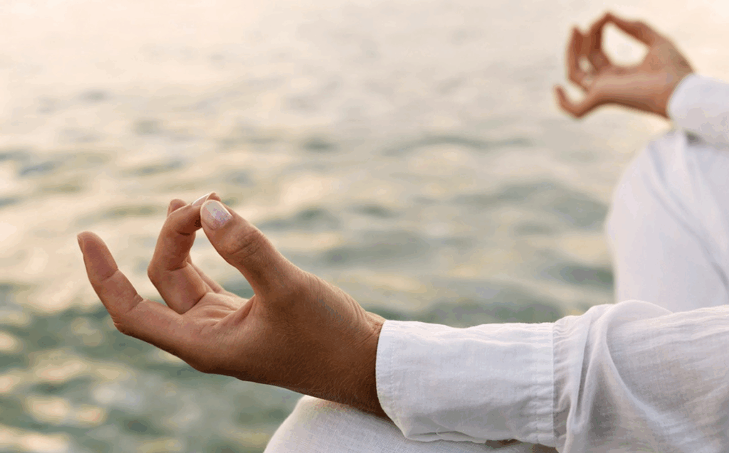 person meditating near water wearing a white linen shirt.