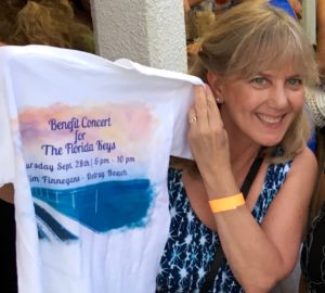 Lady wearing a blue dress smiling holding up a concert tshirt.