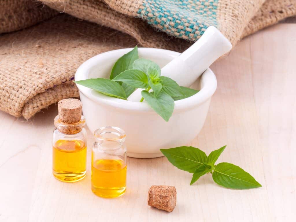 A pestle with herbs next to oil in a tincture jar with burlap behind it.